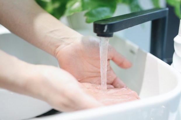 Person washing hands at white sink with black tapware