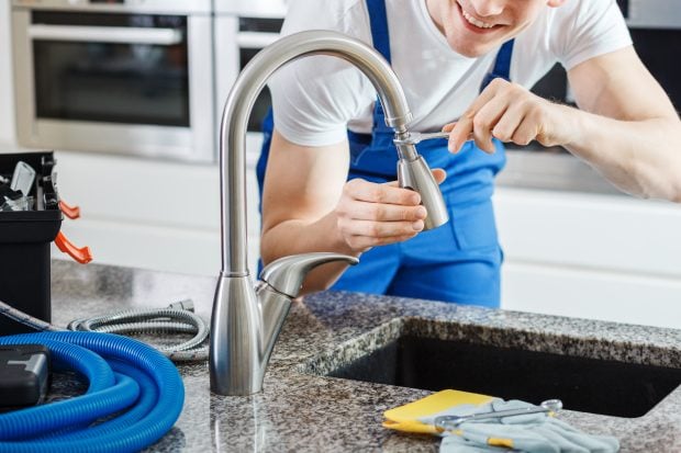 Close-up of smiling plumber fixing a faucet with blue pipes on the countertop Close-up of smiling plumber fixing a faucet with blue pipes on the countertop