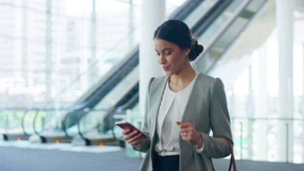 4k video footage of an attractive young businesswoman sending a text while walking through her office building