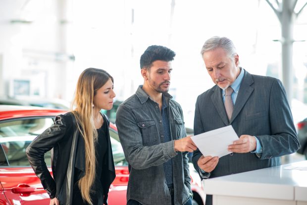 Happy young family talking to the salesman in a car showroom