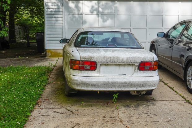 Rear view of an extremely dirty white car in a driveway in front of a white garage door