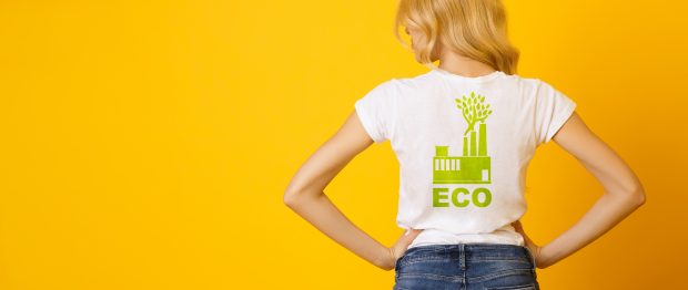 Ecology Concept. Rear View Of Blond Girl Wearing White T-Shirt With Green Eco Print, Standing With Hands On her Hips Over Yellow Background, Panorama