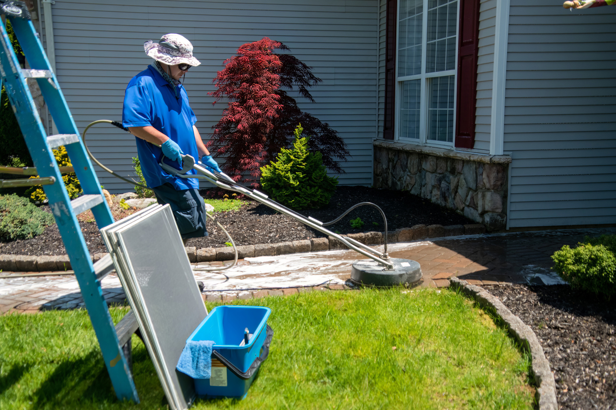 Handyman using a circular power washer to clean a brick walkway in front of a house