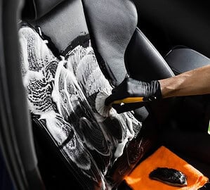 Person washing a car with soap and water, detailing the exterior for a spotless, shiny finish during car cleaning