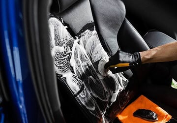 Person washing a car with soap and water, detailing the exterior for a spotless, shiny finish during car cleaning