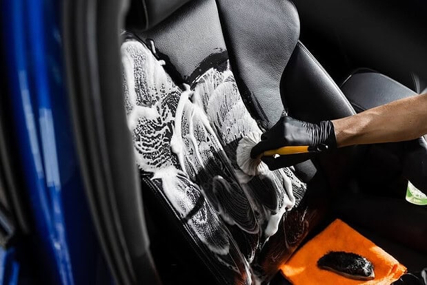 Person washing a car with soap and water, detailing the exterior for a spotless, shiny finish during car cleaning