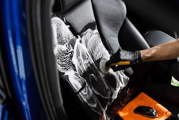 Person washing a car with soap and water, detailing the exterior for a spotless, shiny finish during car cleaning
